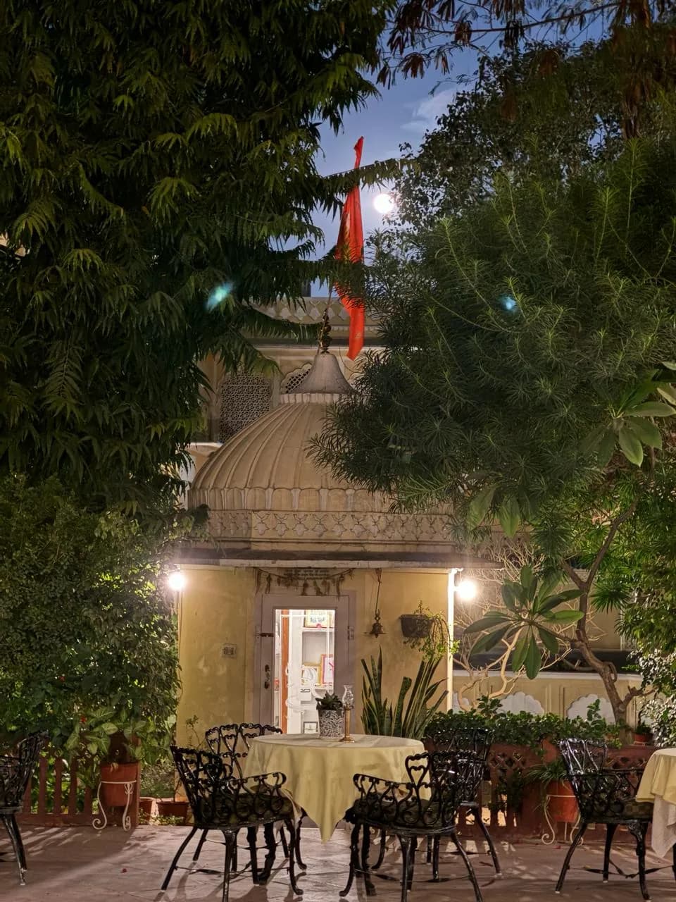 A lamplit pavilion and garden tables in a heritage hotel courtyard