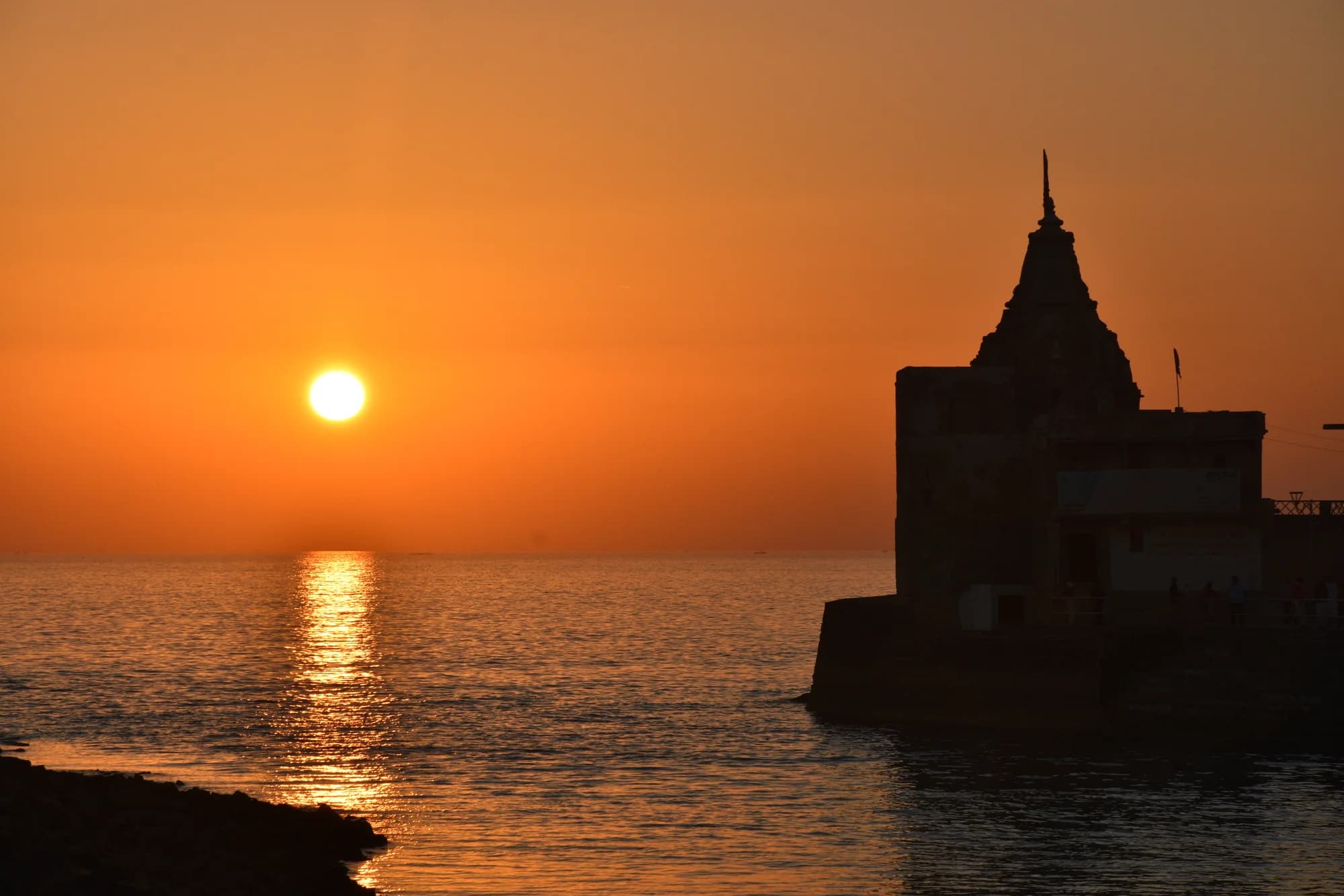 The sun setting over the Arabian Sea beside a temple silhouette at Dwarka